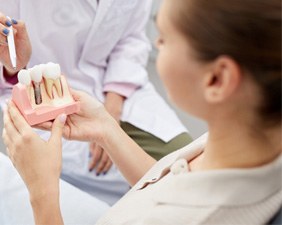 A patient holding a dental implant model while a dentist talks with them