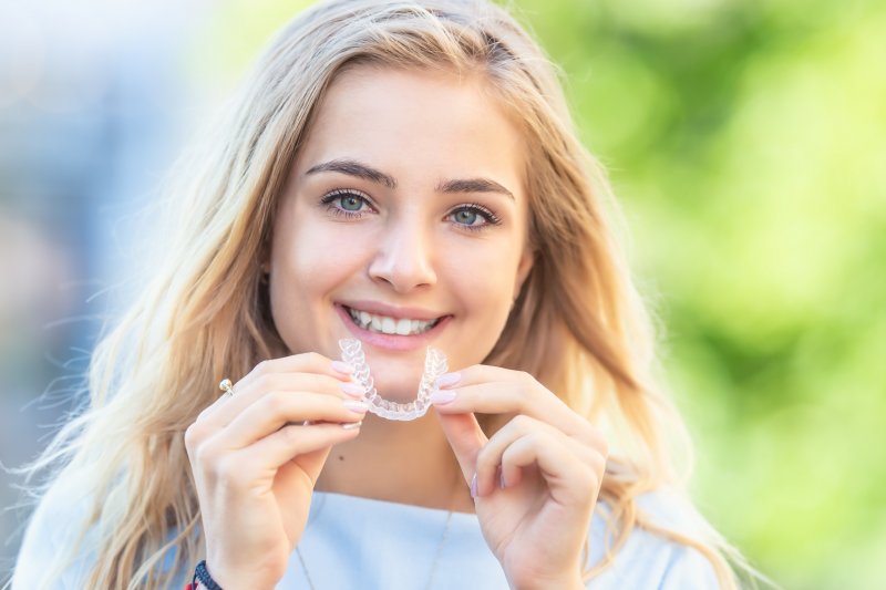 A young blonde woman holding an Invisalign aligner outdoors
